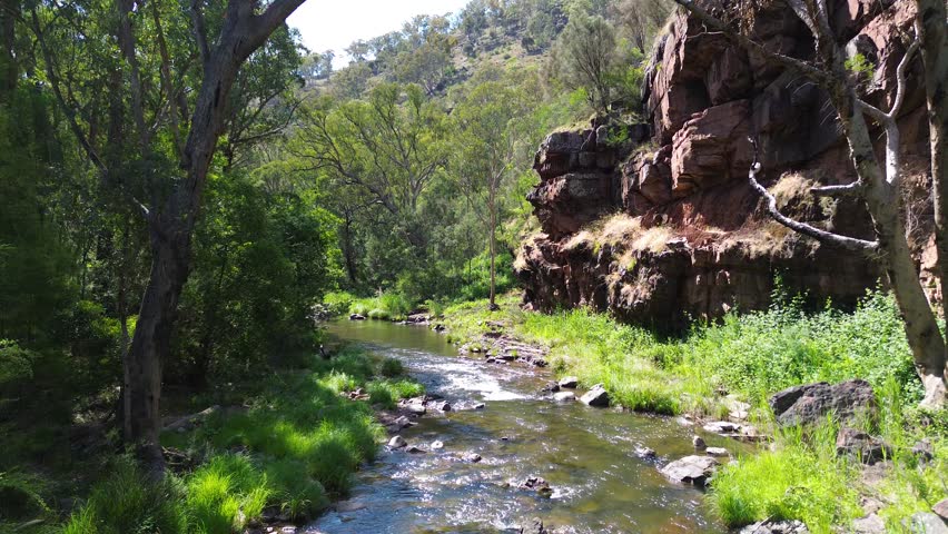 Aerial moving forward over high country stream with cliffs in the Australian mountains.