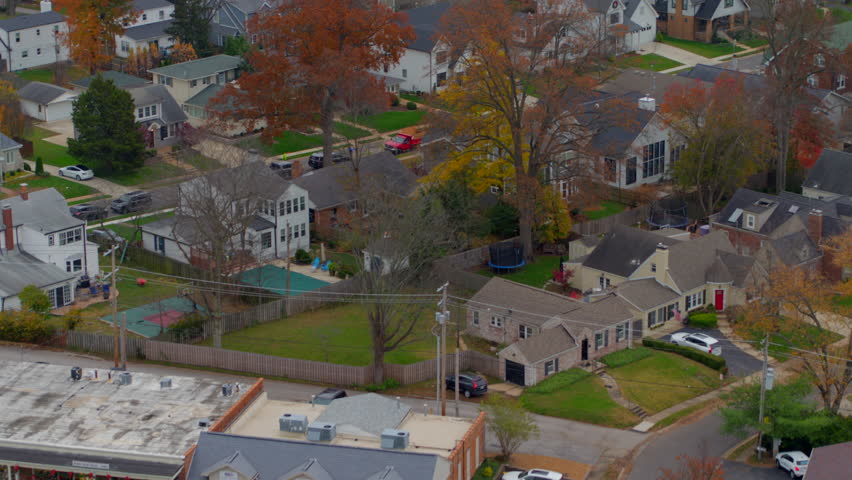 Beautiful aerial flying over a charming subdivision in the Midwest during autumn. Captures vibrant fall foliage, cozy homes, and a car driving down the street. Perfect for suburban themes.