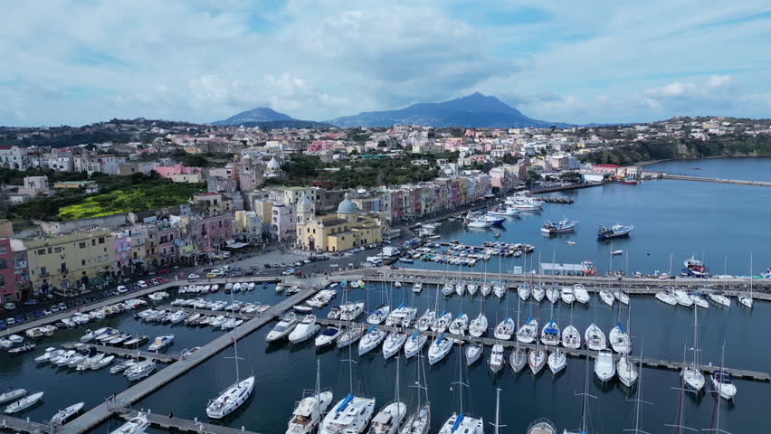 Flying over marina towards historic church and buildings of Procida, a popular holiday island in Italy
