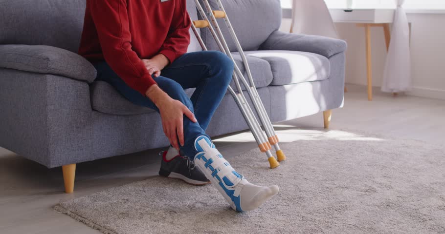Man with broken leg trying to walk using his crutches in living room at home. Disabled male person with plastered leg in rehabilitation and recovery having fractured limb. 4k video.