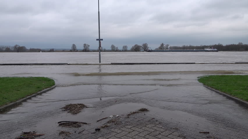 Abstract shot of flooded road and cargo boats sailing on the Rhine river in Tolkamer, high water levels in the Netherlands
