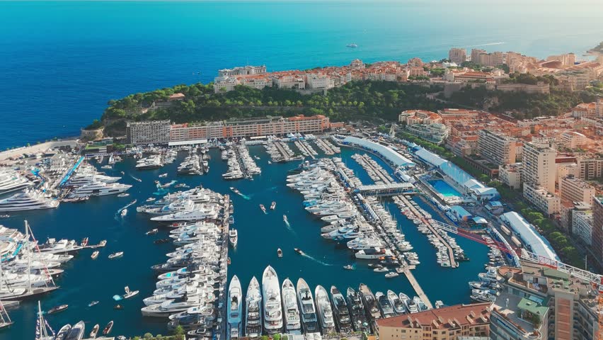 Aerial view of the city center of the Principality of Monaco. The scene showcases luxury yachts moored in Monaco Bay, the Palais Princier de Monaco, and luxury apartment buildings of Monte Carlo 
