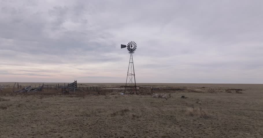 Lone windmill stands in vast Texas prairie under cloudy sky, evoking solitude