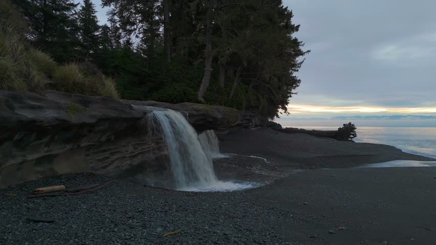 Tranquil waterfall on a black sand beach at dusk on Vancouver Island, British Columbia, Canada. Serene nature scene.