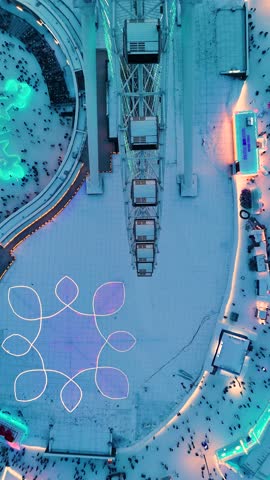 Vertical flyover top-down drone shot of the Snowflake Ferris wheel at the Harbin Ice Festival at sunset, China