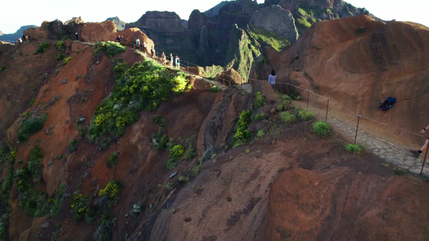 Flyover of brunette hiker navigating toward the iconic Stairway to Heaven trail on the Pico Ruivo hike in Madeira, Portugal. Aerial 4k drone view surrounded by dramatic drop-offs on both sides.