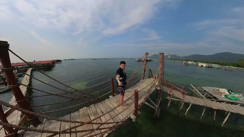 A guy is standing on a bridge in the middle of water.