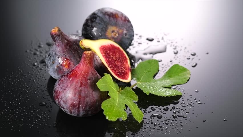 Fig fruit. Ripe sweet fresh figs fruits with leaves close up, on black background with water drops. Healthy sweet Mediterranean organic fruits. Vegan food. Slow motion. 