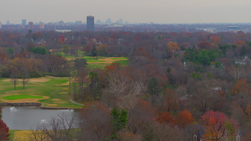 Beautiful aerial flying away from a golf course and over trees at peak autumn color in Ladue, St. Louis, Missouri. Captures vibrant foliage, serene suburban charm, and the Clayton skyline.
