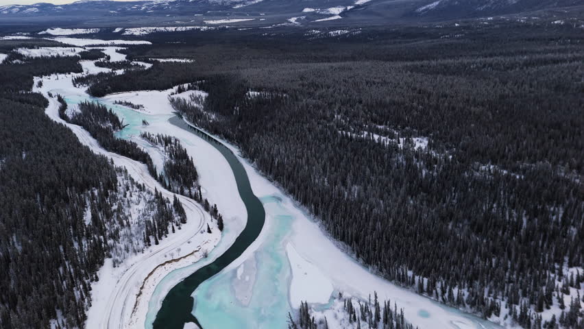 The Takhini River Flowing Through a Winter Landscape, Framed by Dense Forest and Snow-covered Mountains in Yukon, Canada - Aerial Drone Shot