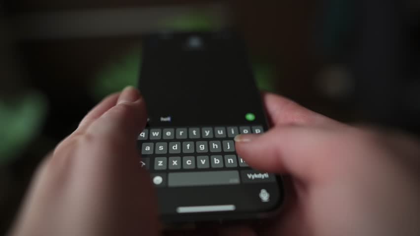Hands Deleting Message on Smartphone Keyboard person deletes typed message on smartphone, with fingers pressing touchscreen keyboard dimly lit background adds modern and focused feel