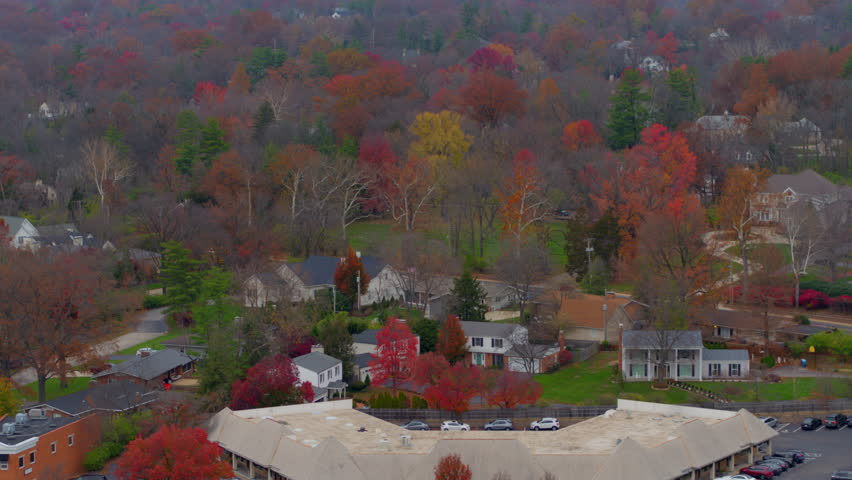 Stunning aerial toward elegant houses surrounded by trees at peak autumn color in the Ladue neighborhood of St. Louis, Missouri. Captures vibrant foliage and serene suburban charm.