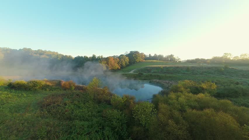 Aerial drone view of misty pond surrounded by lush greenery rolling hills in Johnson City, Tennessee, at sunrise warm sunlight fog create tranquil scenic atmosphere Misty Pond Rolling Hills at Sunrise