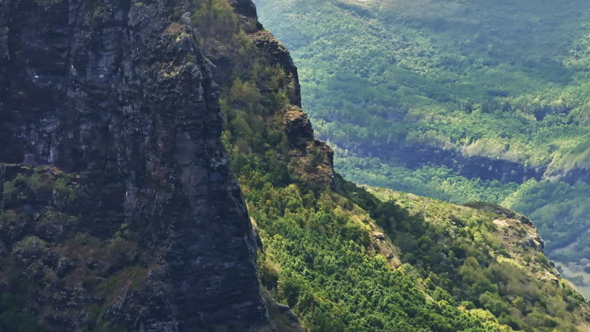 Le Morne Brabant mountain peak, Mauritius, with expansive ocean views and lush tropical landscape, aerial orbit around steep cliffs with cloud shadows
