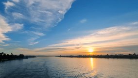 A stunning Nile River sunset with golden sunlight reflecting on calm blue waters, near Luxor, Egypt. A small boat glides peacefully, framed by palm trees and a distant cityscape. - Powered by Shutterstock - Get 15% off with code: PIKWIZARD15