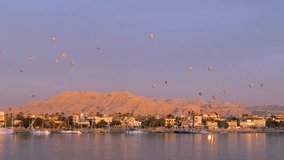 A breathtaking Nile River dawn with golden sunlight illuminating blue waters, Luxor's city, and hills, Egypt. Colorful hot air balloons float in the sky, captured from a cruise. - Powered by Shutterstock - Get 15% off with code: PIKWIZARD15