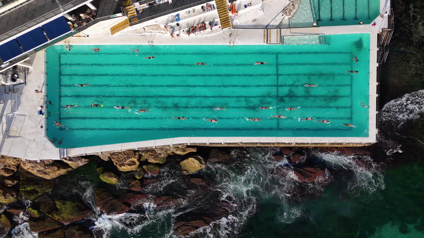 Downward angle drone shot of Bondi Beach’s ocean pool, showcasing swimmers enjoying the stunning seaside setting.