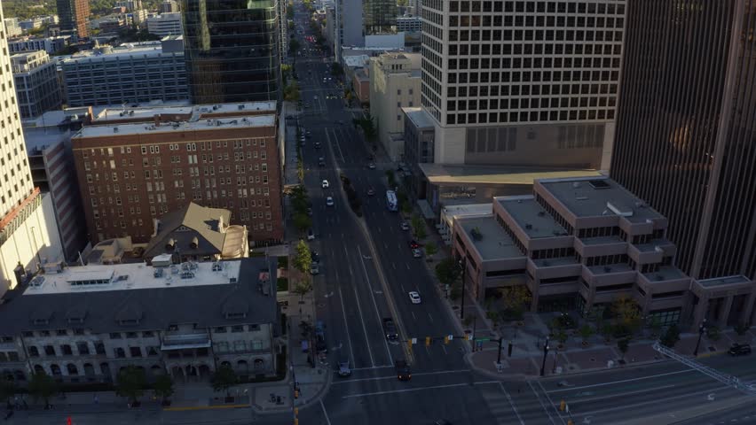 Aerial drone shot of downtown Salt Lake City, tilt up dollying in over State Street. Skyscrapers, apartments, and offices line the street, with fall trees glowing under a golden-orange autumn sunset.