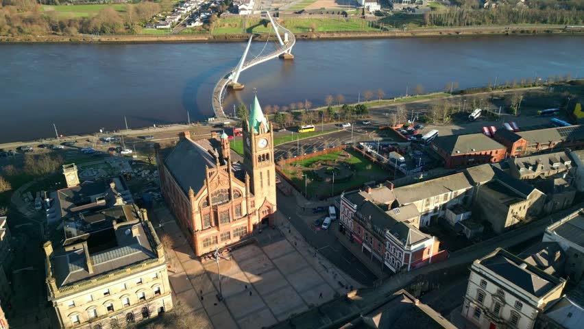 High, forward travelling aerial shot of the Peace Bridge, the Guildhall and the River Foyle in Derry-Londonderry, NI on a bright and sunny day. Filmed in 4K at 60fps and in Rec709 color space.