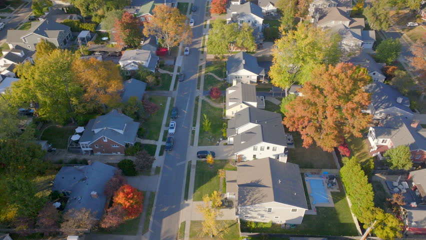High-quality aerial over a nice neighborhood street in Ladue, St. Louis, Missouri, with middle-class houses surrounded by vibrant fall foliage. Features a drift and tilt down.