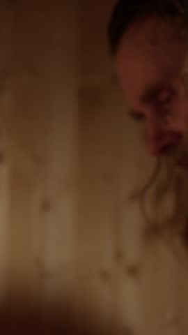 Scruffy man pours water on hot stones steaming up wooden sauna. Vertical