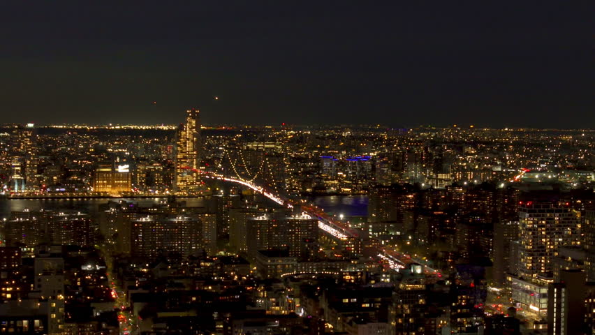 Night view of New York City with illuminated buildings and streets, featuring the iconic Brooklyn bridge and skyscrapers that define the city