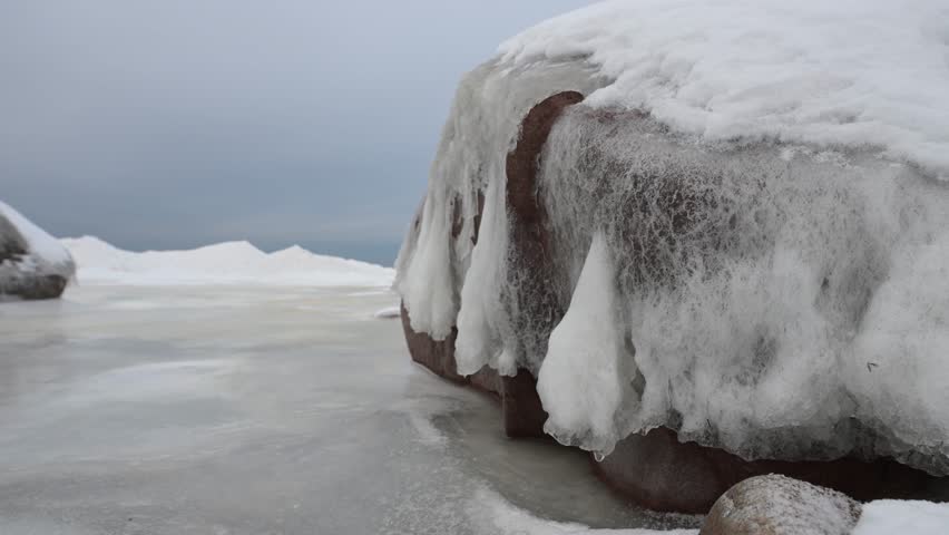 Snenic icy seashore with a boulder covered in ice and snow.