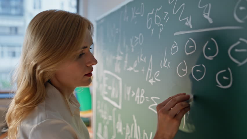 School teacher solving math equations on blackboard with chalk closeup. Focused woman writing formulas on chalkboard classroom. Professional female educator teaching algebra unknown college students - Powered by Shutterstock - Get 15% off with code: PIKWIZARD15