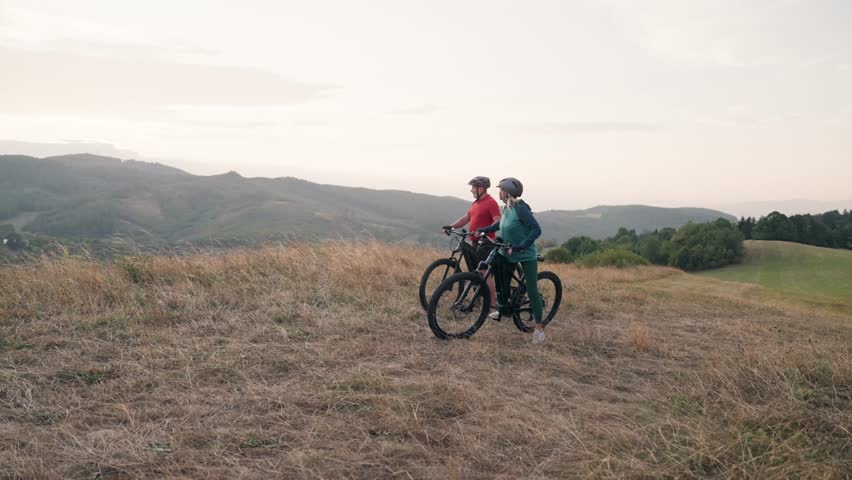 Senior couple on bike ride in autumn nature, enjoying beautiful view from hill. Older active people on electric bikes.