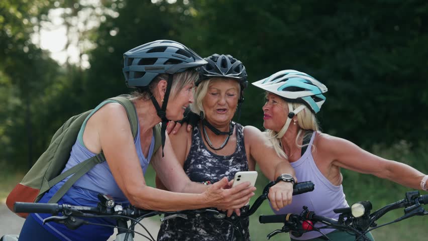 Senior friends on bike tour in nature taking selfie. Older women on low impact route riding electric bikes.