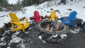Four colorful Adirondack chairs surround a stone fire pit with wood inside, set in a snowy outdoor scene with a path and natural rock features - Powered by Shutterstock - Get 15% off with code: PIKWIZARD15