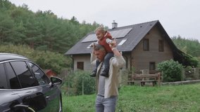 Father playing with son carry him on shoulders by electric car and in front of house with solar panels on rooftop. - Powered by Shutterstock - Get 15% off with code: PIKWIZARD15