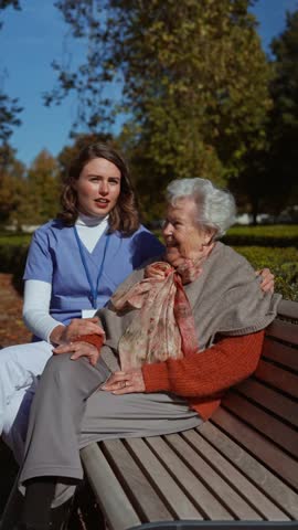 Elderly woman sitiing on bench and talking with her nurse, sharing her problems with female caregiver.