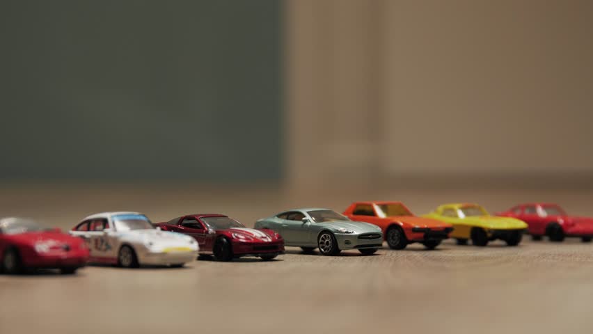 A playful scene of toy cars lined up on a wooden floor with a small crash