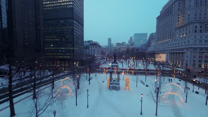 FPV drone glides over snowy Place du Canada adorned with Christmas decorations, heading toward René Lévesque Blvd W during peaceful winter morning at Square Dorchester, Downtown Montreal.