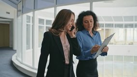 Business colleagues discussing document on go. Smiling woman assisting executive consulting on project. Confident businesswoman talking mobile phone walking office hallway. Corporate people closeup - Powered by Shutterstock - Get 15% off with code: PIKWIZARD15