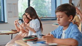 Children enjoying school break sitting classroom desks with gadgets. Little schoolboy playing smartphone game. Classmates using cellphones watching entertaining content together. Kids phone addiction - Powered by Shutterstock - Get 15% off with code: PIKWIZARD15