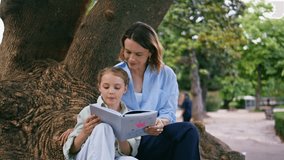 Mother daughter reading book at nature closeup. Adorable little girl woman parent sitting big tree at summer park. Smiling mommy kid resting together spending weekend. Happy family relationships  - Powered by Shutterstock - Get 15% off with code: PIKWIZARD15