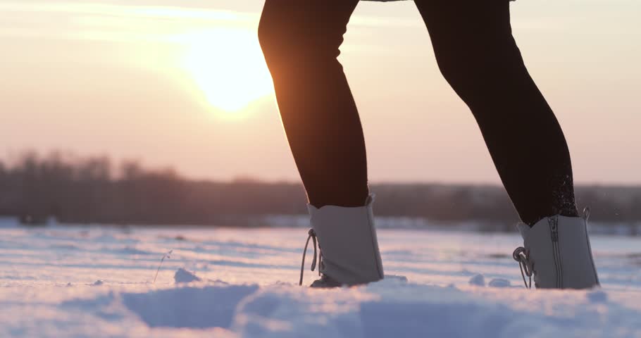 female legs in winter boots confidently walk along snow path sunset. Active recreation winter forest: adventure, frosty air and footprints snow. winter walk beauty snow landscapes and power nature.