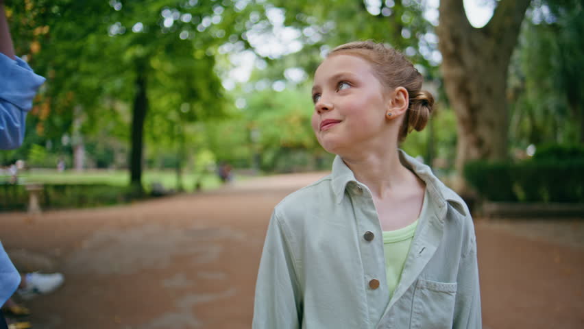 Funny child strolling park talking mommy closeup. Lovely small kid walking alley communicating with unrecognizable female parent. Blonde girl holding anonymous mother hand at alley. Childhood concept 