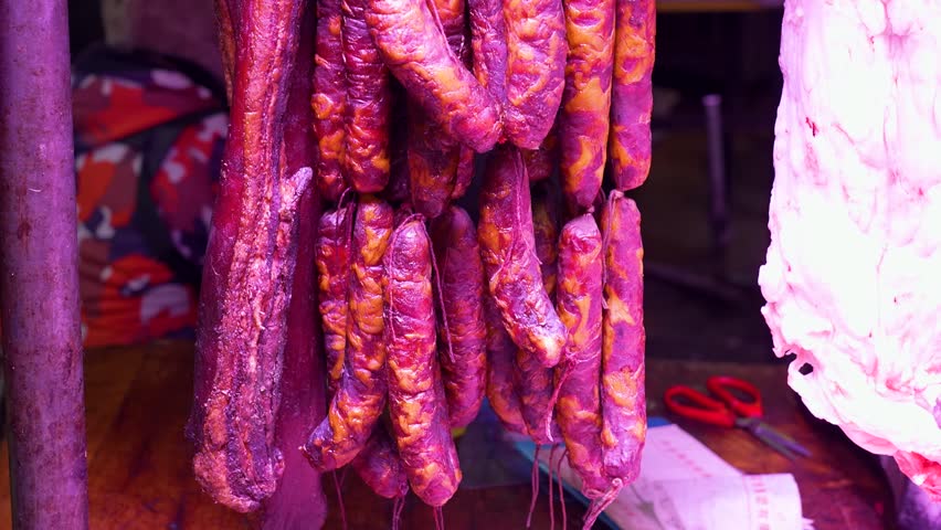 Slow-motion shot of traditional spicy sausages hanging in a vibrant Chongqing market. China