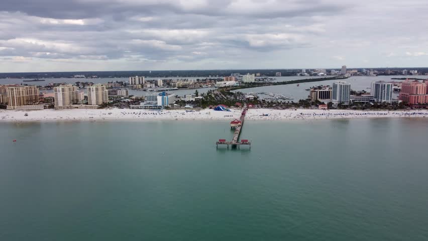 Pier 60 at Clearwater Beach, Florida, United States. Drone video showing the famous Pier 60 extending into the ocean. Crowded beach, clear blue water, and vibrant summer scenery.