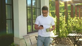 Relaxed mature man standing on terrace in garden drinking coffee checking smartphone in morning sun. Businessman outdoor at home, perfect start of a long business day. Life of successful entrepreneur. - Powered by Shutterstock - Get 15% off with code: PIKWIZARD15