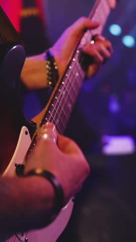 
Concert view of an electric guitar player with vocalist and rock band performing in a club, male musician guitarist on stage with audience in a crowded concert show club hall arena, hands on guitar