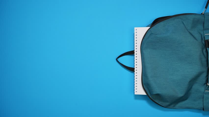 Stop motion animation of colorful school supplies moving to school bag on blue background. Back to school concept. Top view