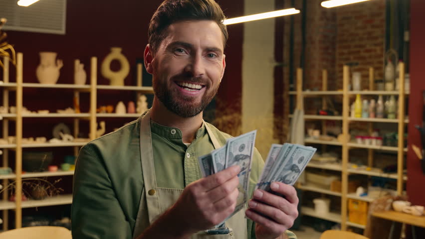 Rich wealthy happy Caucasian man male businessman guy small business owner entrepreneur potter apron counting money dollars winning cash salary finance wage budget payment wealth inside pottery store