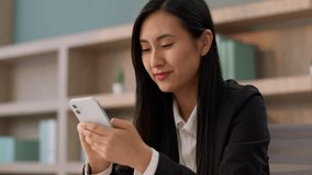 Smiling positive Asian Japanese girl office worker secretary business woman joyful Korean female businesswoman entrepreneur looking smartphone screen using mobile phone chat app typing message indoor - Powered by Shutterstock - Get 15% off with code: PIKWIZARD15