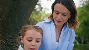 Little kid reading novel spending free time with mom together at green garden portrait. Caring mother enjoying fairytale story with daughter resting at weekend. Woman girl staring book near big tree - Powered by Shutterstock - Get 15% off with code: PIKWIZARD15