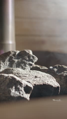 Steam rise from heated rocks as copper sauna ladle pours water on, vertical