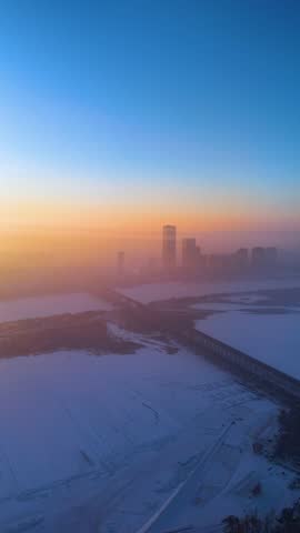 Vertical aerial drone shot of the Harbin City skyline with the frozen Songhua River at sunrise, China